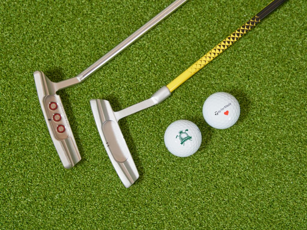 Two golf putters and golf balls placed on artificial turf, ideal for practice.