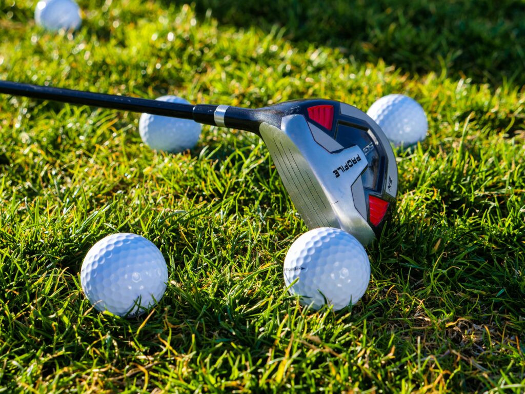Close-up of a golf club with multiple golf balls on lush grass, ideal for sports themes.